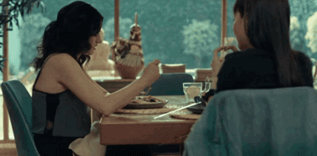 two women sit at a table with plates of food and drinks