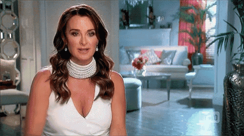 a woman in a white dress and pearls is sitting in a living room .