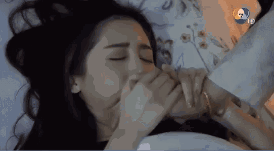 a woman is laying in bed with her eyes closed while a man holds her hand over her mouth ..