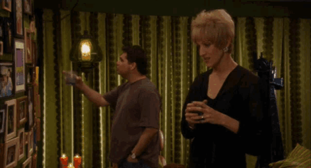 a man and a woman are standing in front of a wall of pictures and the woman says " you know mary tyler moore "