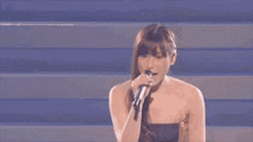 a woman in a strapless dress is singing into a microphone on stage .
