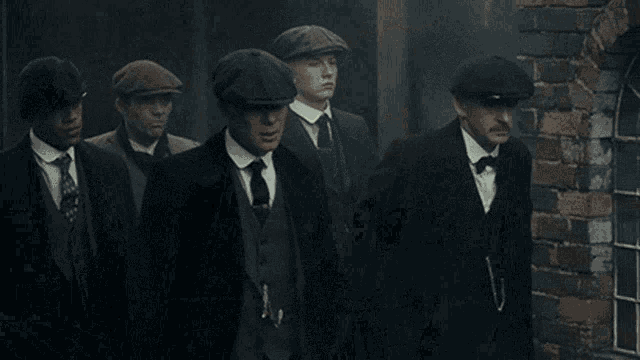 a group of men in suits and hats are walking down a city street