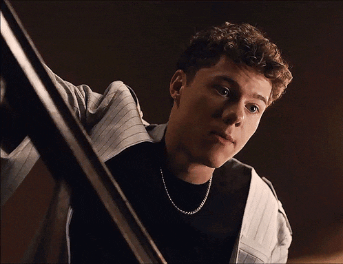 a young man with curly hair wearing a black shirt and a silver chain