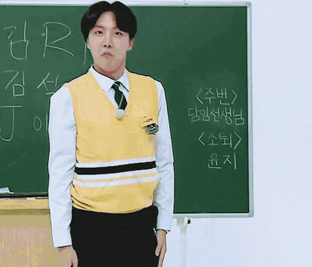 a man wearing a yellow vest and tie stands in front of a blackboard that says j.r.