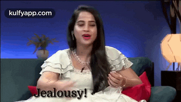 a woman in a white dress is sitting on a couch and says jealousy !