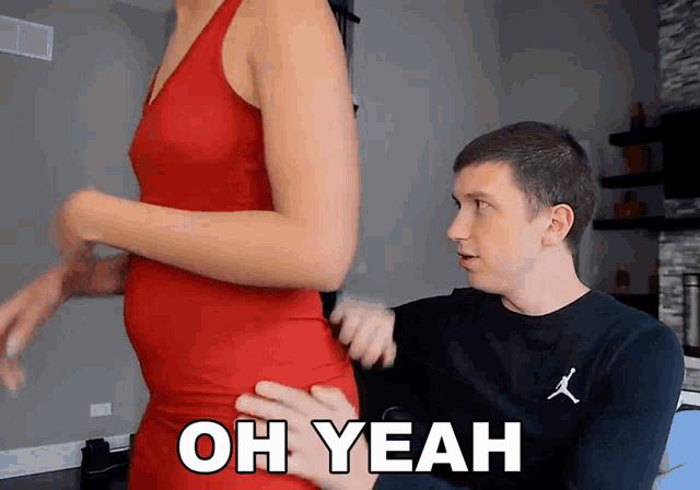 a woman in a red dress is being touched by a man in a black shirt with the word oh yeah on it