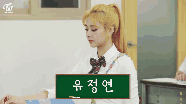 a girl in a ponytail sits in front of a chalkboard with korean writing on it
