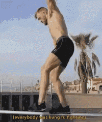 a shirtless man is jumping over a railing with the words " everybody was kung fu fighting " written below him