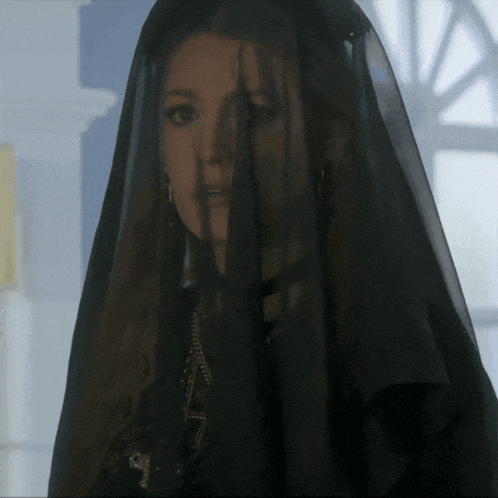 a woman wearing a black veil is standing in front of a window