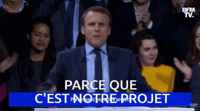 a man in a suit and tie stands in front of a crowd and says " parce que c 'est notre projet "