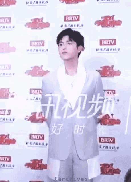 a young man in a suit is standing in front of a wall with chinese writing .