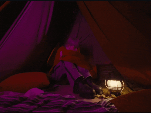 a person is sitting in a tent with a lantern on the floor