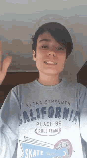 a young boy wearing a california sweatshirt is smiling and waving .