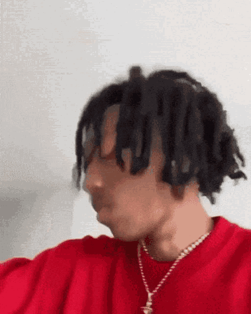 a man with dreadlocks is wearing a red sweater and a gold chain .