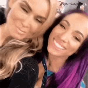 two women are posing for a picture together and smiling for the camera . one of the women has purple hair .