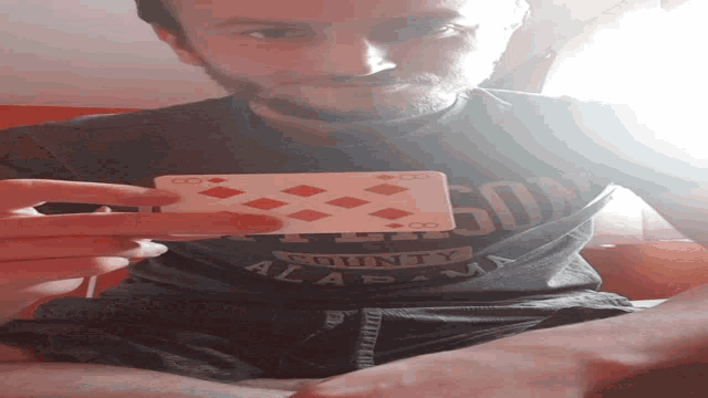 a man wearing an alabama county shirt holds a playing card