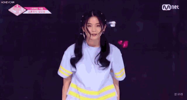 a girl in a white shirt with yellow stripes is dancing on a stage with her arms outstretched .