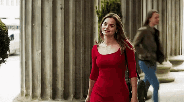 a woman in a red dress is walking down the street with a man walking behind her .
