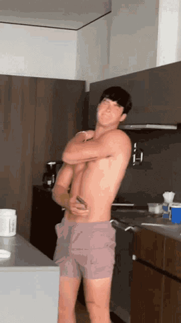 a shirtless man in shorts is standing in a kitchen with his arms crossed