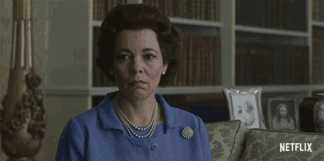 a woman wearing a blue shirt and pearls sits on a couch with a netflix logo on the bottom