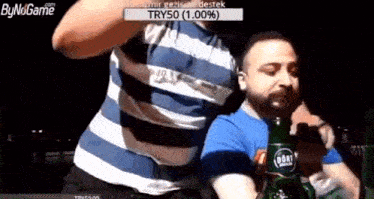 a man in a striped shirt is holding a bottle of beer while another man looks on .