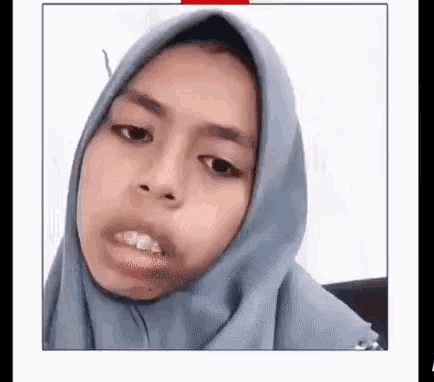 a woman wearing a hijab is making a funny face and looking at the camera .