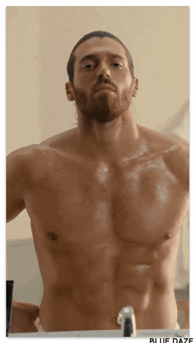 a shirtless man looks at himself in the mirror