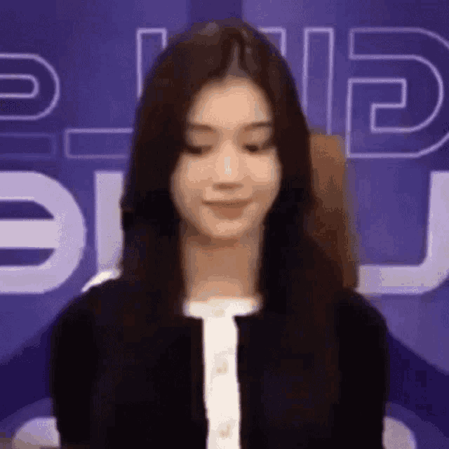 a woman with long black hair is standing in front of a sign that says ' g ' on it .