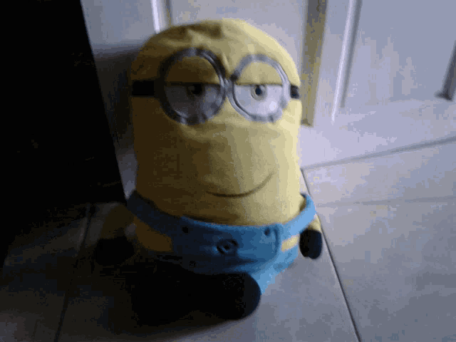 a stuffed minion with glasses and blue shorts is sitting on a tile floor