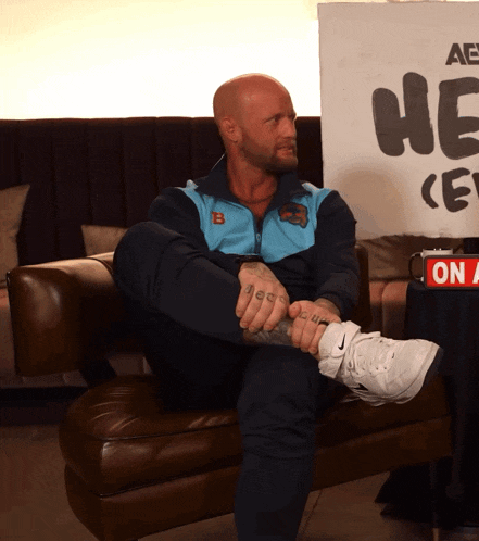 a man is sitting on a couch in front of a sign that says " he "