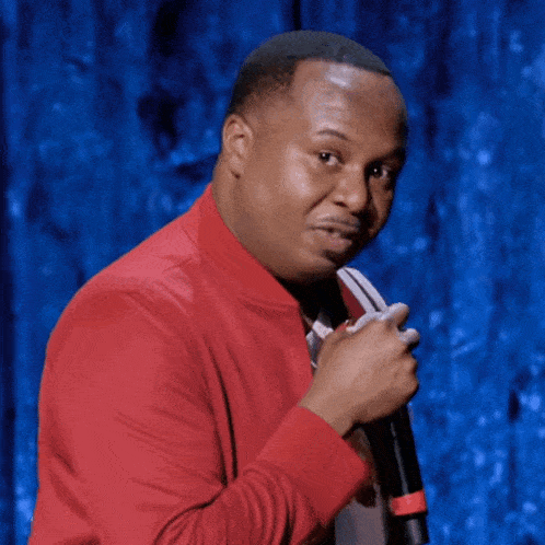 a man in a red jacket is holding a microphone in front of a blue curtain