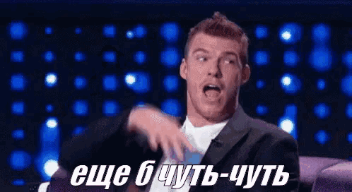 a man in a suit and tie is sitting on a couch and making a funny face with russian writing behind him .