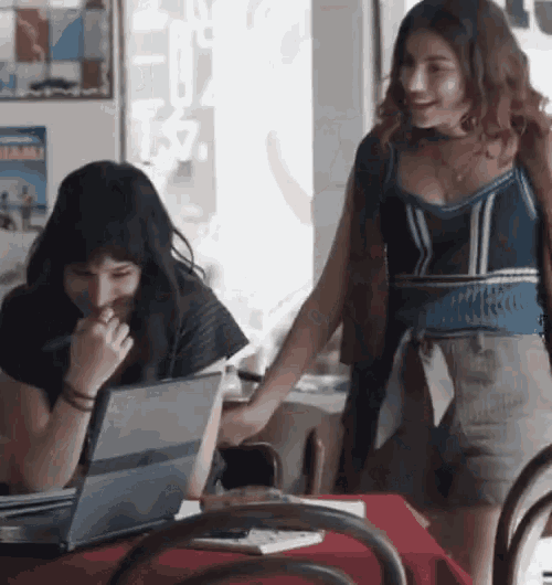 two women are sitting at a table with a laptop and a poster that says miami on it