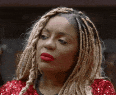 a woman with braids and red lipstick is wearing a red sequined shirt