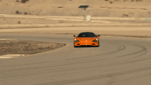 an orange sports car is driving down a road with trees in the background