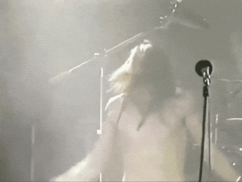 a shirtless man singing into a microphone with his arms in the air