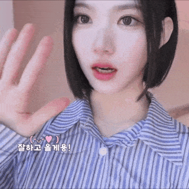a woman wearing a blue and white striped shirt is making a hand gesture