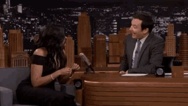 a woman in a black dress is sitting next to a man in a suit who is clapping .
