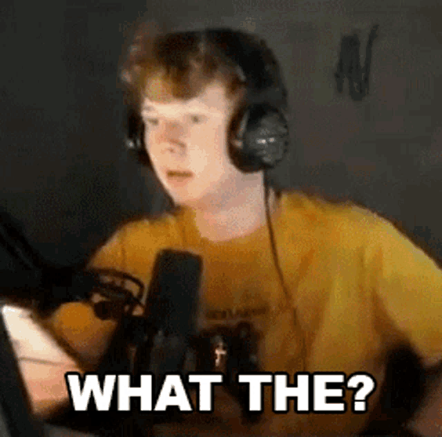 a young man wearing headphones is sitting in front of a microphone and looking at a cell phone .