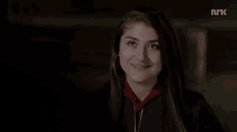 a woman wearing hoop earrings and a black jacket is smiling in a dark room .