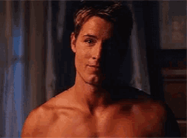 a shirtless man is standing in front of a window looking at the camera