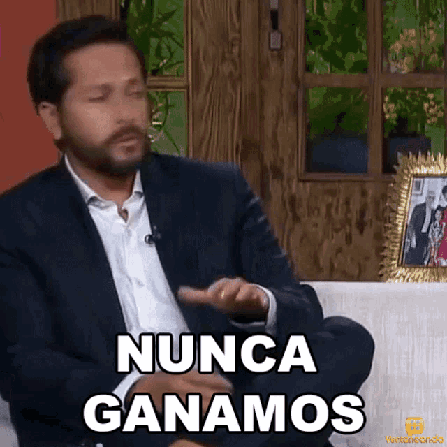 a man in a suit is sitting on a couch and saying " nunca ganamos "