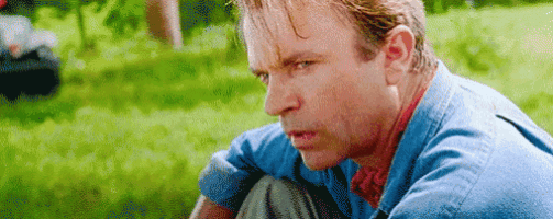 a man in a blue shirt is sitting in the grass looking at something .