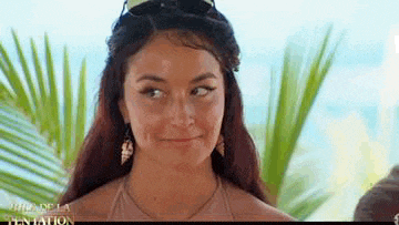 a woman wearing sunglasses and earrings is standing in front of a palm tree and smiling .
