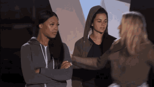 three women are standing with their arms crossed and one has a hoodie on