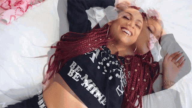 a woman with red hair is laying on a bed wearing a be mine shirt