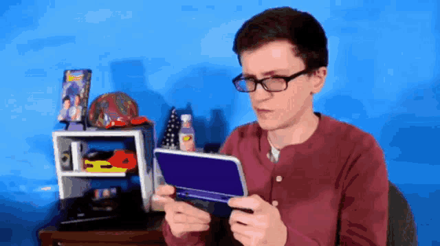 a young man wearing glasses is holding a nintendo 3ds