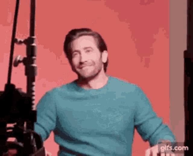 a man in a blue sweater is standing in front of a pink background .