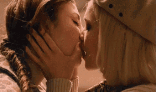 two women are kissing each other with one wearing a beret .