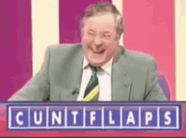 a man in a suit and tie is sitting in front of a sign that says ' cuntflaps ' on it .